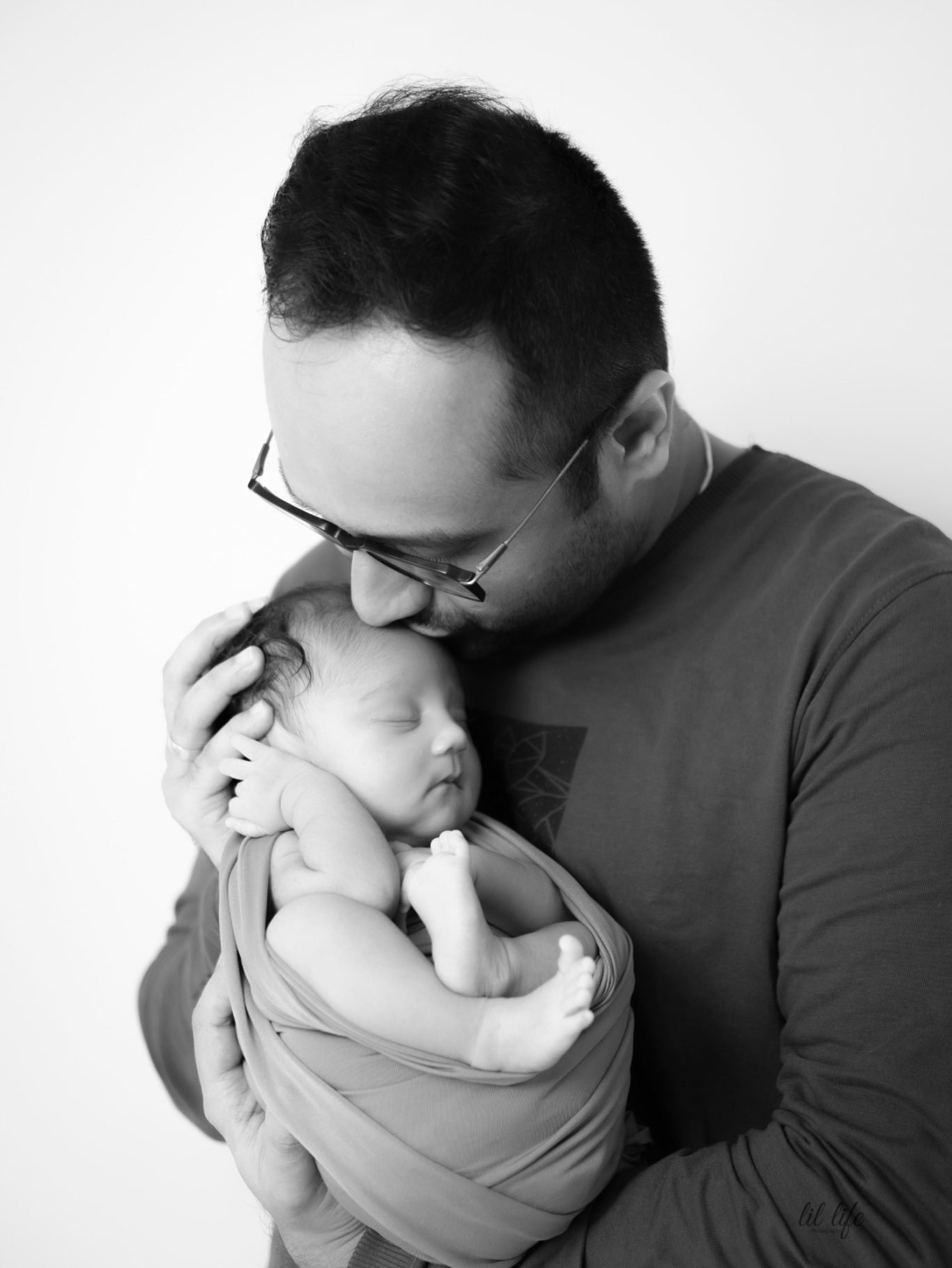 A man gently holds and kisses a sleeping baby wrapped in a blanket.
